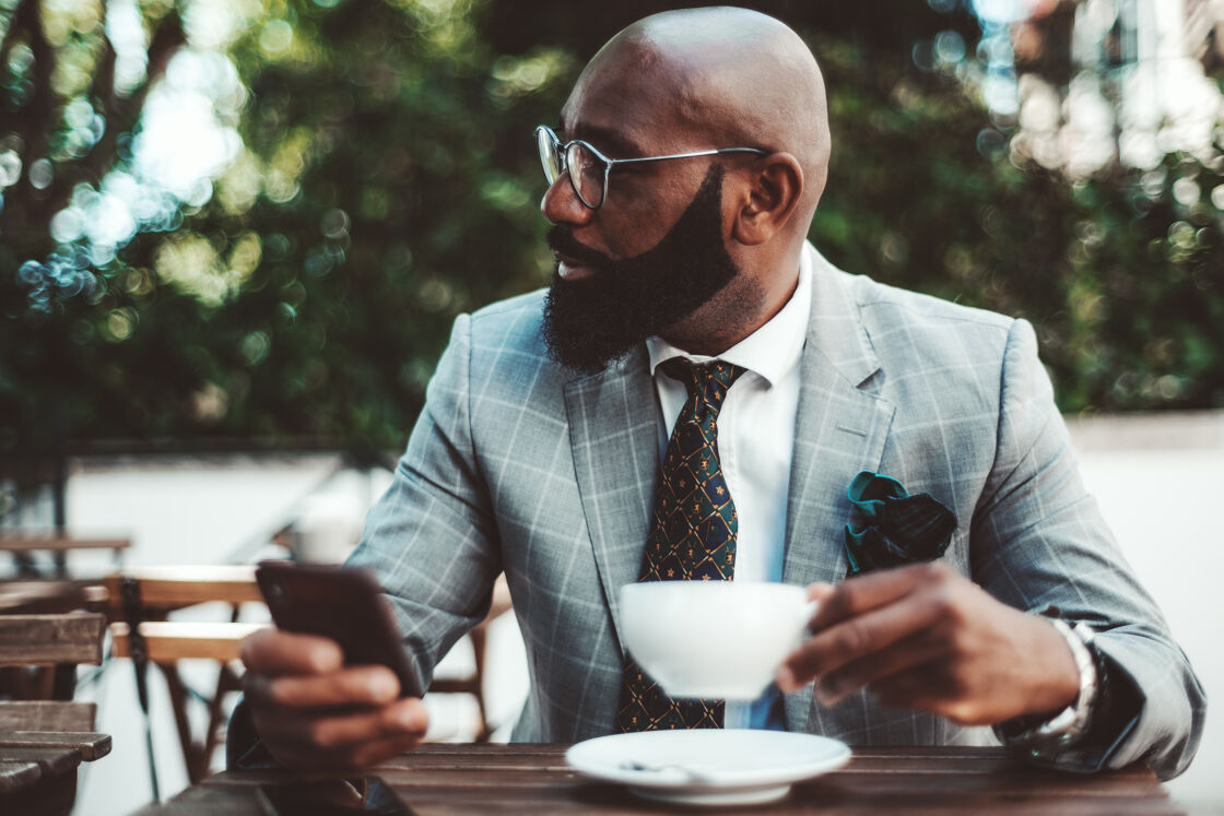 Black man in a grey suit looking to the side and holding tea.