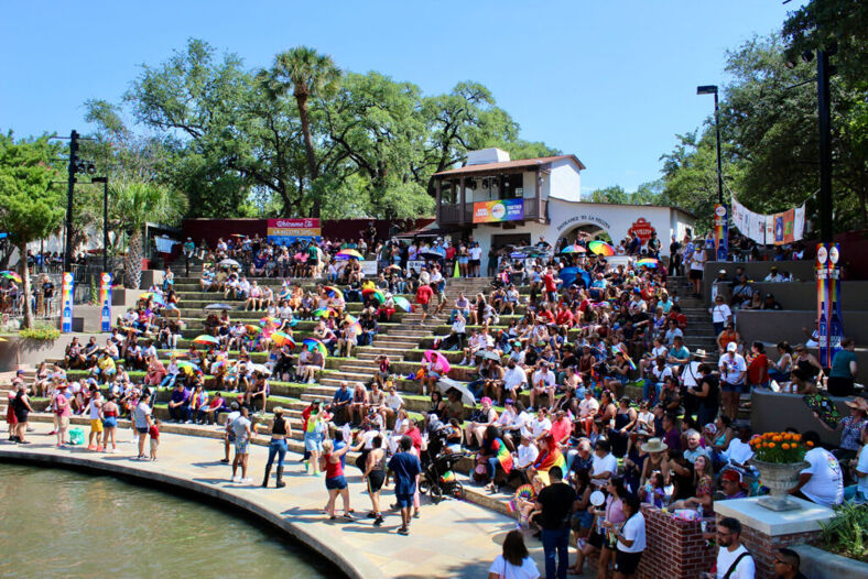 A large group gathers on outdoor steps to watch a show by the river