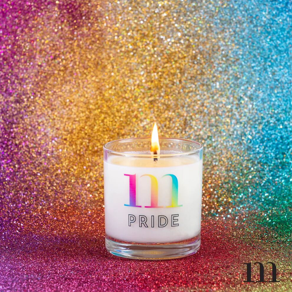 A white candle in front of a glittery backdrop with a rainbow "m" and the word "Pride" at the bottom.