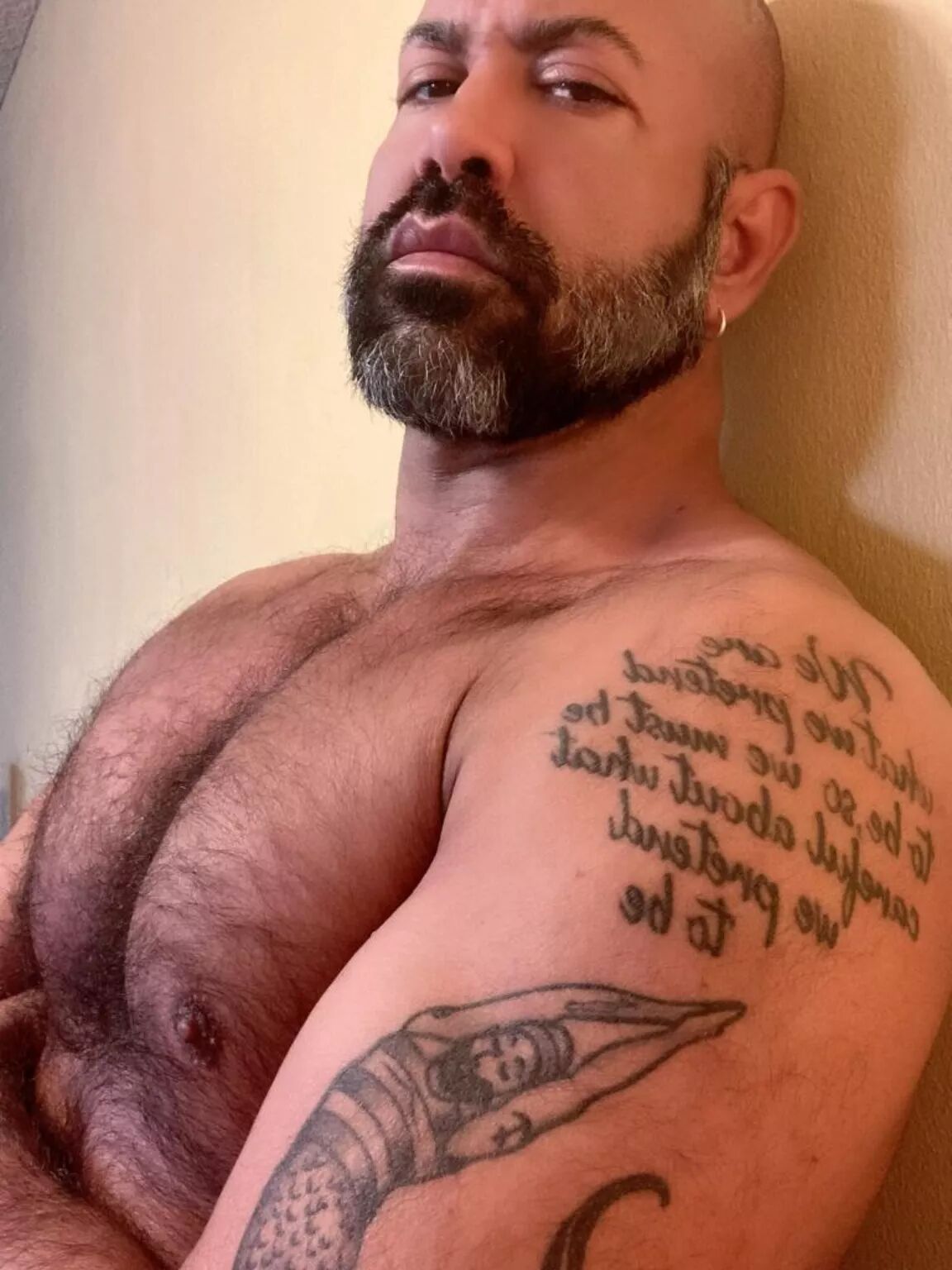A sultry bearded bear with a tattooed shoulder smolders at the camera