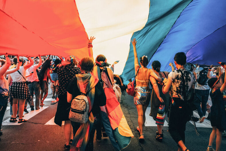 A group of people under a giant rainbow flag.
