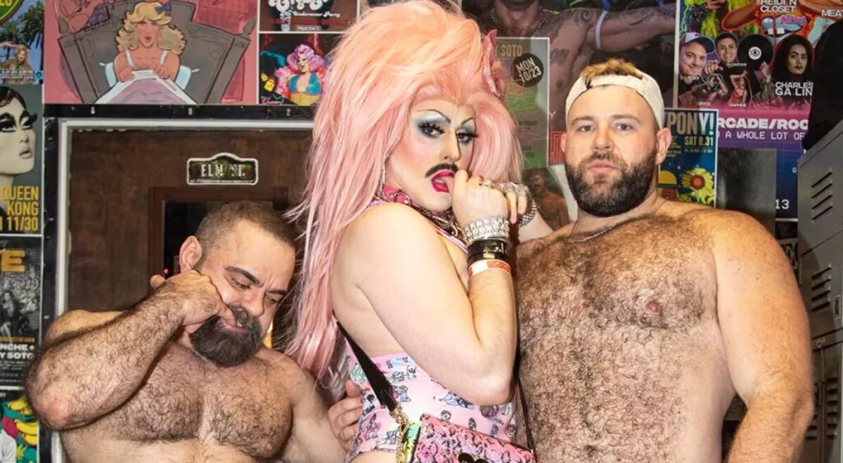 Two shirtless bears and a drag queen with bright pink hair