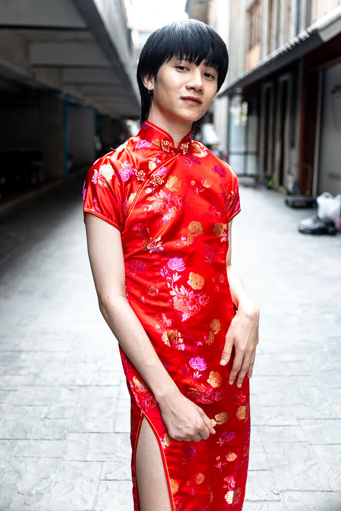 A person with short drak brown hair wears a traditional red brocade thai dress.