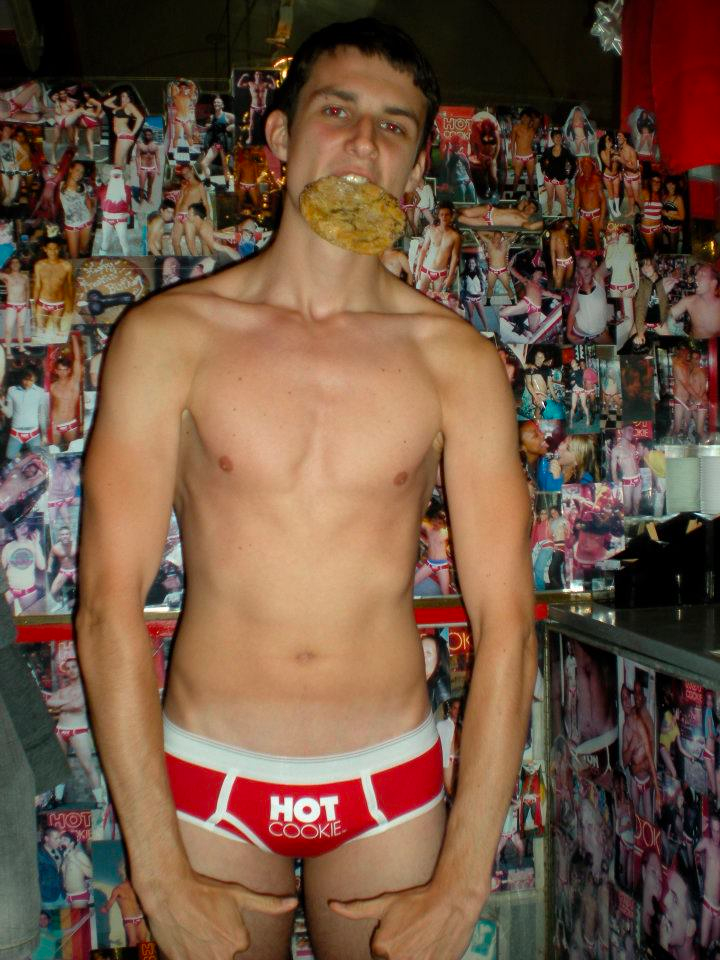 A man in red underwear with a cookie in his mouth.