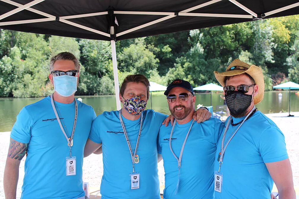 Four volunteers wearing masks stand in front of a beautiful river