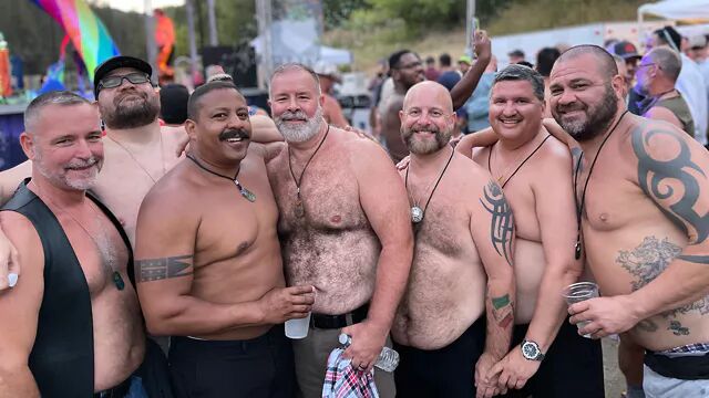 A group of hunky, shirtless men smile at the camera
