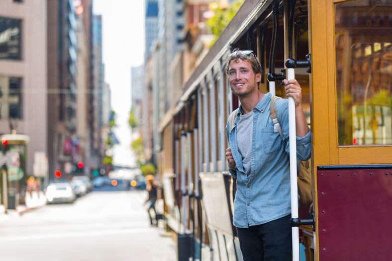 Man in a denim button-up shirt riding cable car in San Francisco.