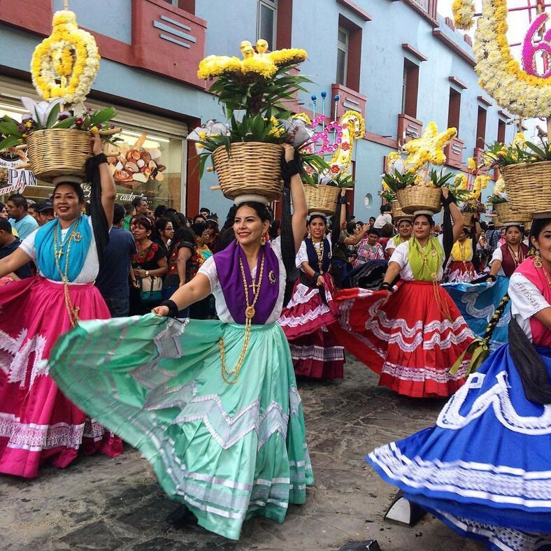 Traditional dancers wearing colorful skirts hold baskets on their heads in Oaxaca City.