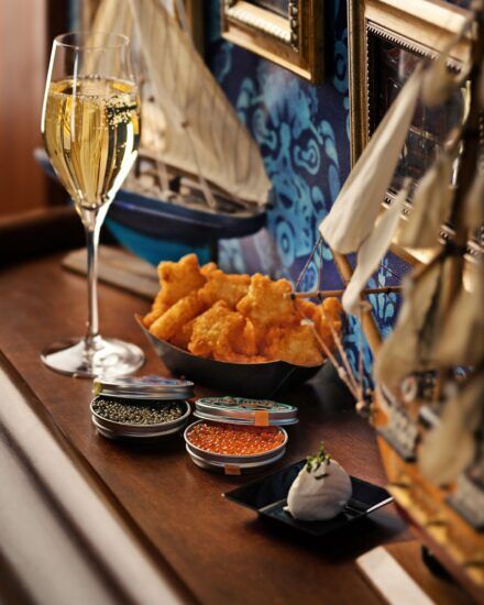 A glass of champagne next to a basket of star shaped tater tots and caviar