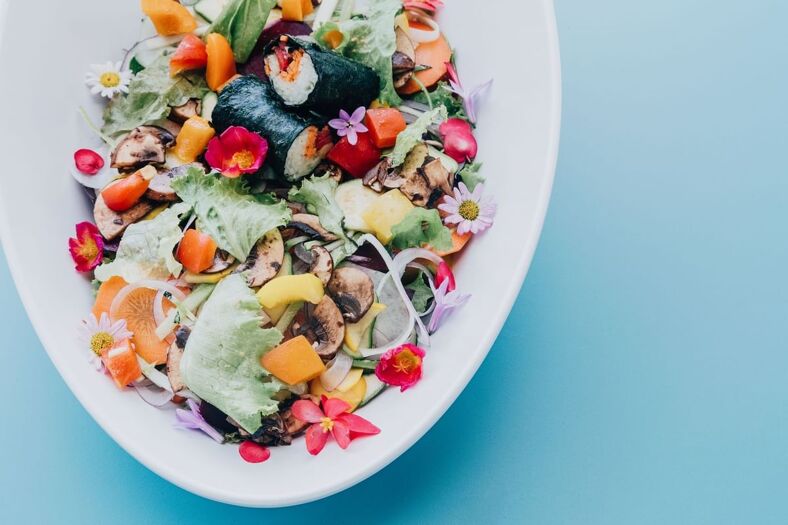 A colorful salad with fruits, vegetables, and edible flowers.