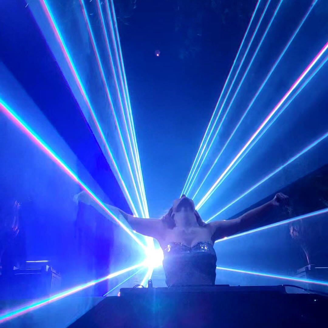 DJ performs in front of bright lights in a nightclub.