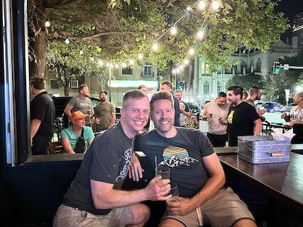 Two friends sitting on an outdoor patio enjoying beers.