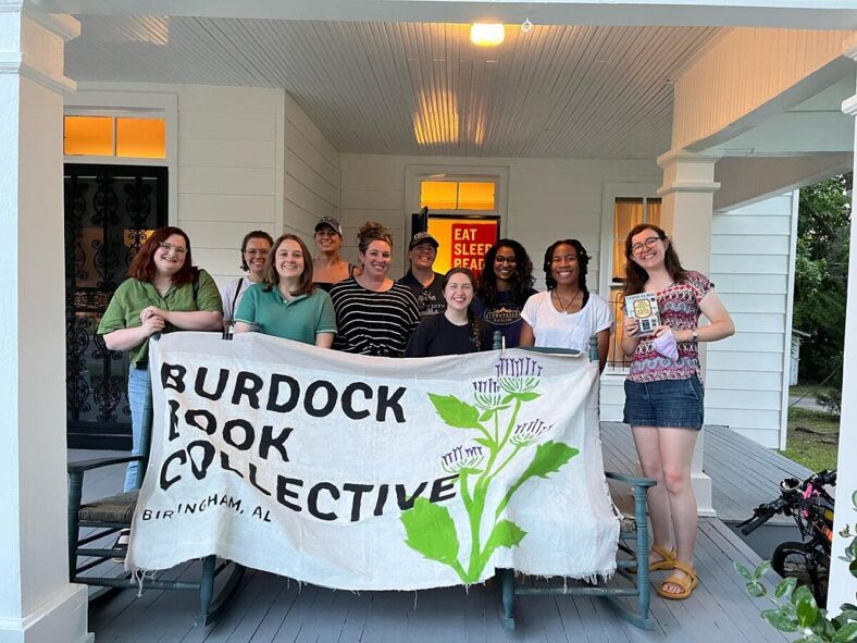 A group of ten people smiling and holding a Burdock Book Collective banner.
