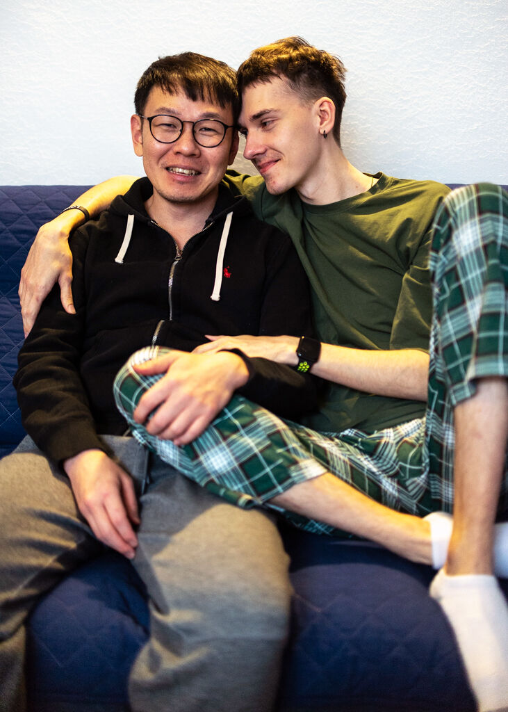 Two men in pajamas cuddle on the couch.