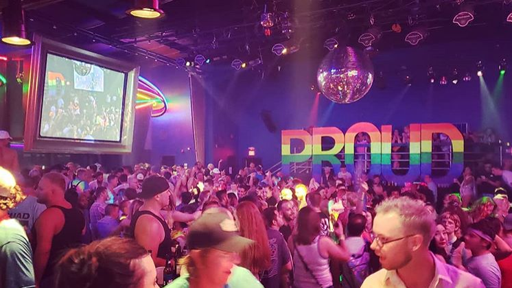 A packed dance floor with a huge rainbow signage that spells out PROUD. Photo via anglesokc.com