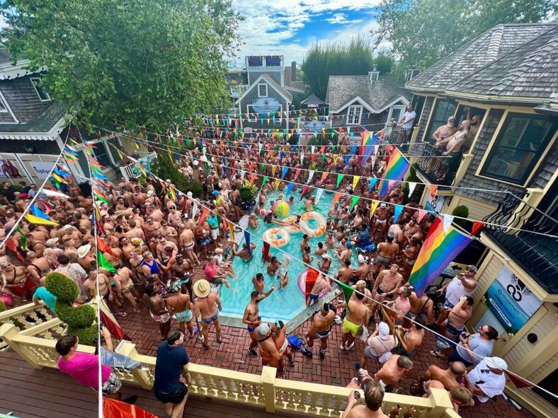 Giant pool party. Rainbow flags hang from balconies over the packed pool. Dozens of men socialize, swim and drink.