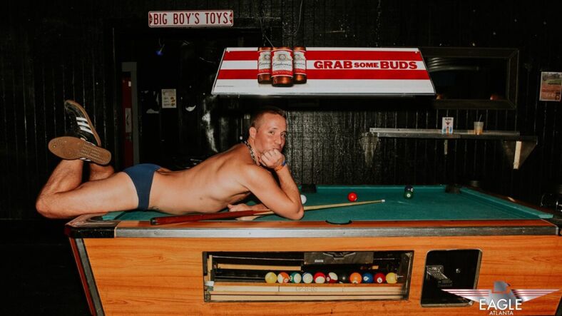 A cheeky man down to his underwear lays flirtatiously on a pool table. Photo via Atlanta Eagle
