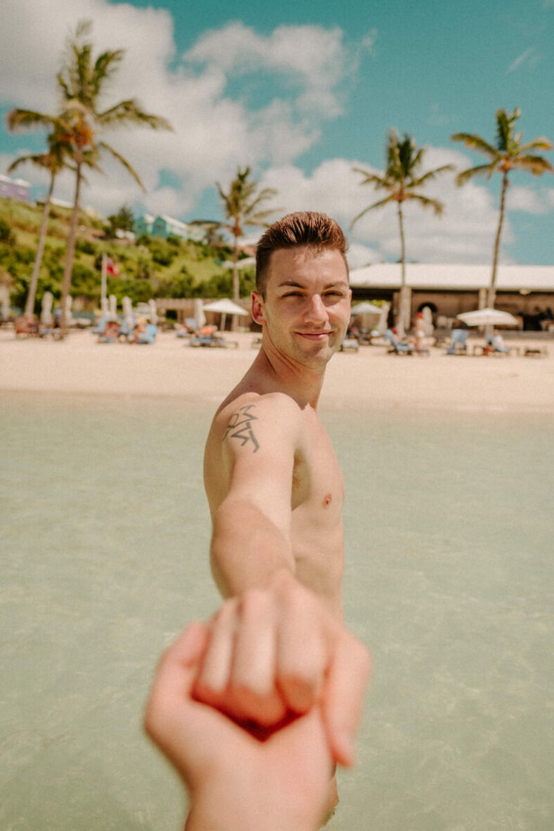 Man on the beach holds hand of lover off camera.