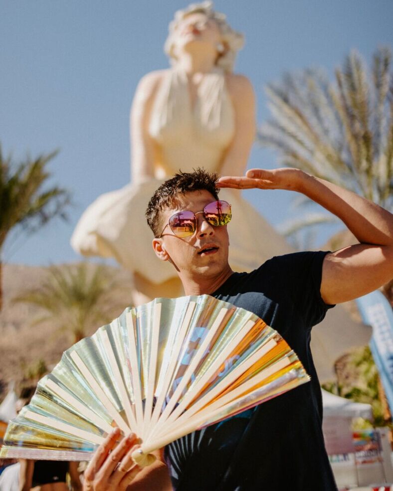 A man wearing sunglasses holds a fan in front of a statue in Palm Springs