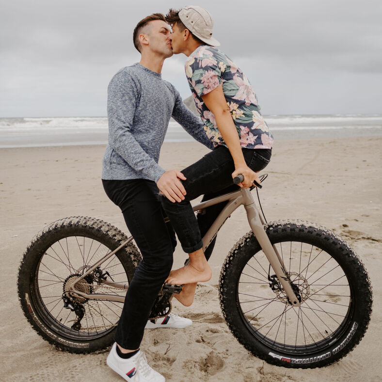 Michael and Matt kissing on a bike on the Oregon Coast