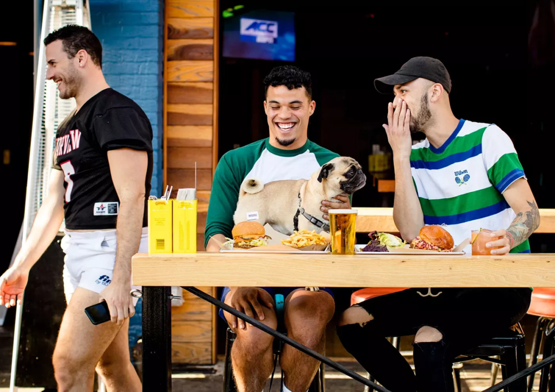 Guys sitting at a sports bar eating burgers and drinking beer.