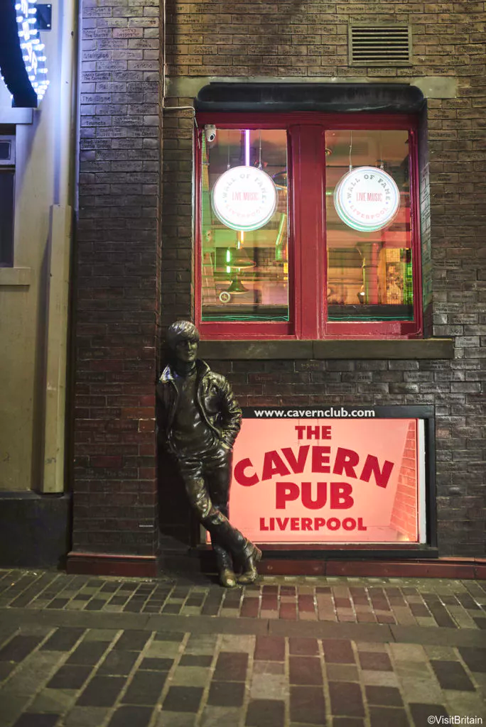 A wax sculpture of John Lennon rests against a red sign for Cavern Pub, in Liverpool UK