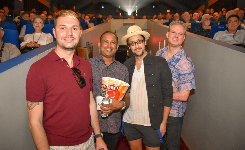 A group of men at OUTshine Film Festival in Fort Lauderdale standing in the entrance hall of a packed movie theater. One holds popcorn and a water as if ready for the show.