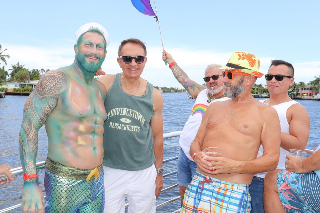 A group of men of different ages partying at Floatarama in Fort Lauderdale. One of them is covered in shimmery makeup and wearing scaled tights to look like a merperson.