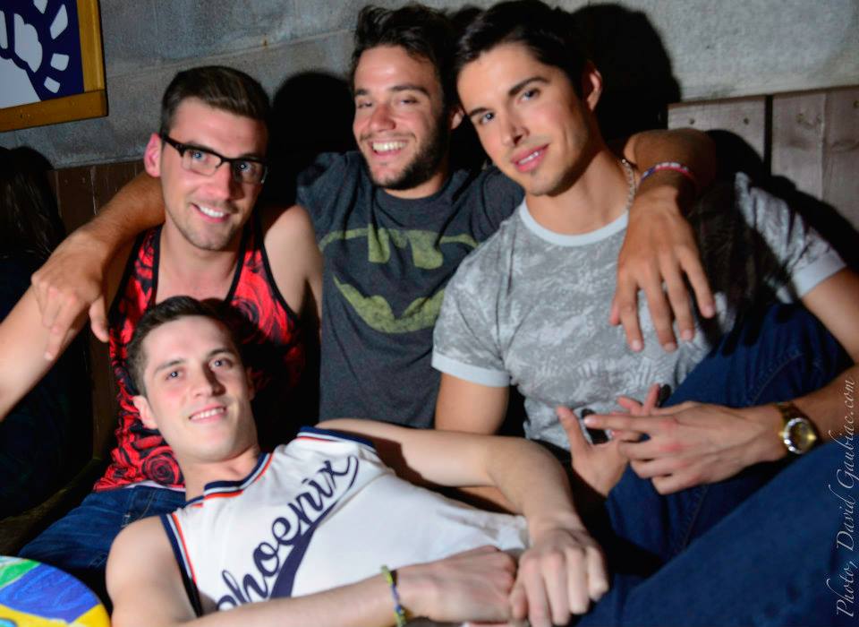 Four handsome men lounge and embrace while smiling at the camera. Photo via Complexe Sky