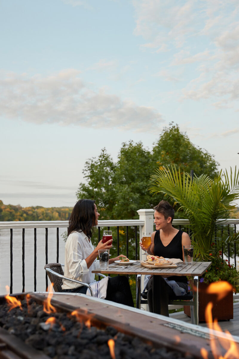 A lesbian couple enjoys wine on a patio overlooking a lake