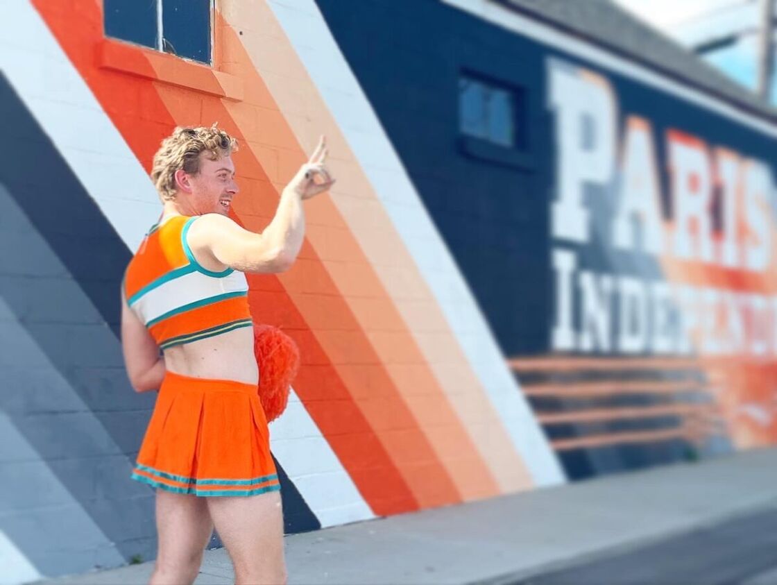 Caudill poses in a cheerleaders top and skirt in front of one of his murals.