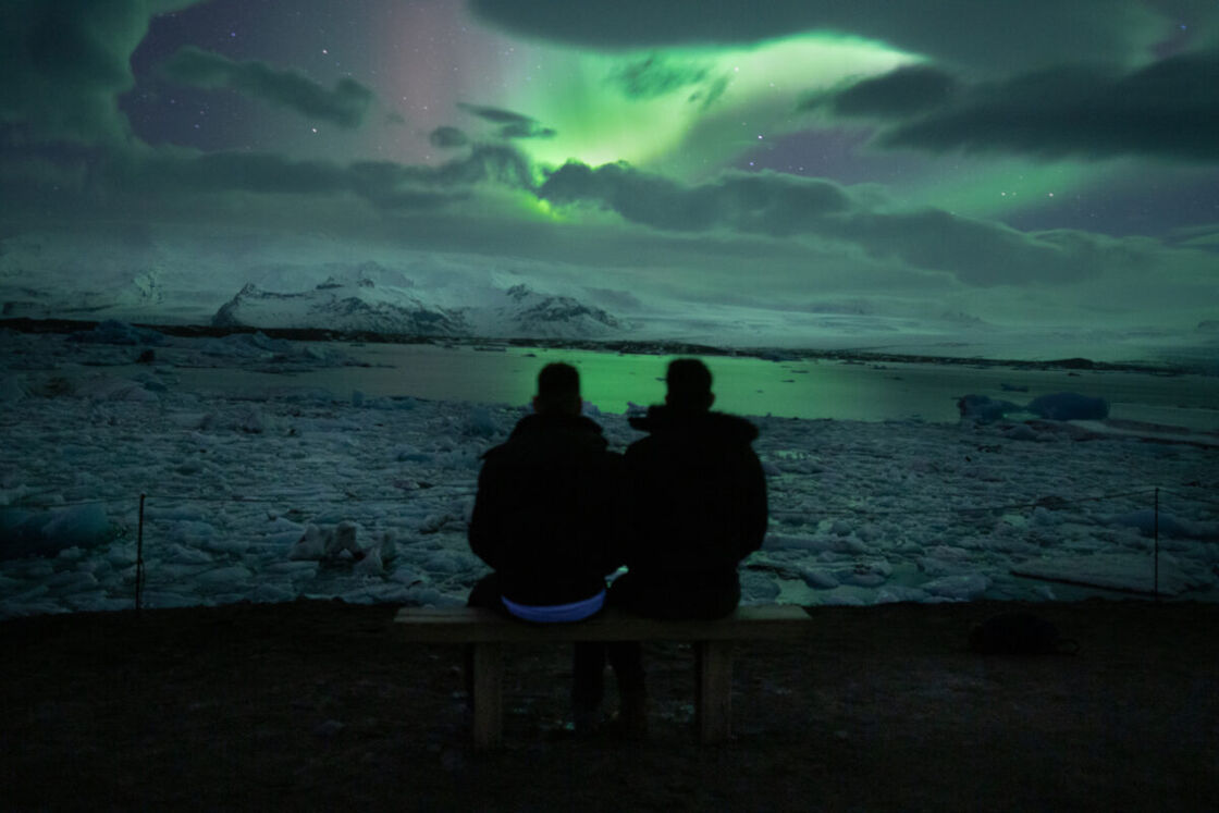 Stafan and Seby sit on the edge of an iceberg and watch the green glow of the Northern Lights.