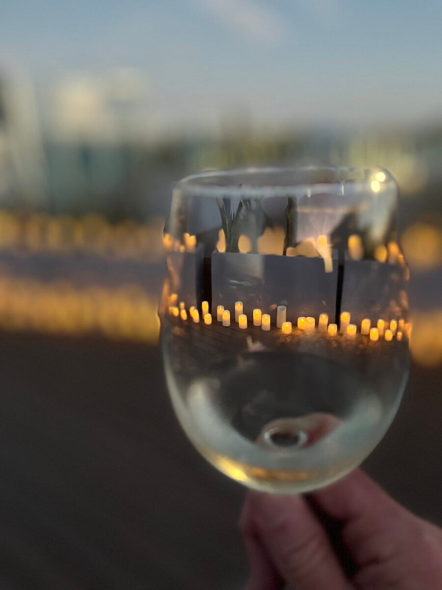 Candles glimmer in the background as seen through a raised glass of white wine.