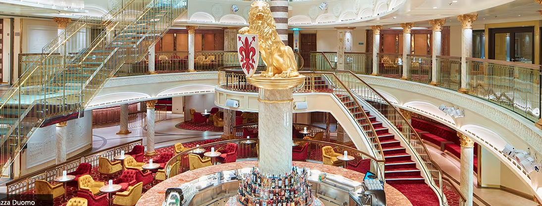 Luxurious multi level bar and restaurant inside Carnival Firenze. Red carped and a golden lion adorn the interior. Photo via Carnival Cruise Line