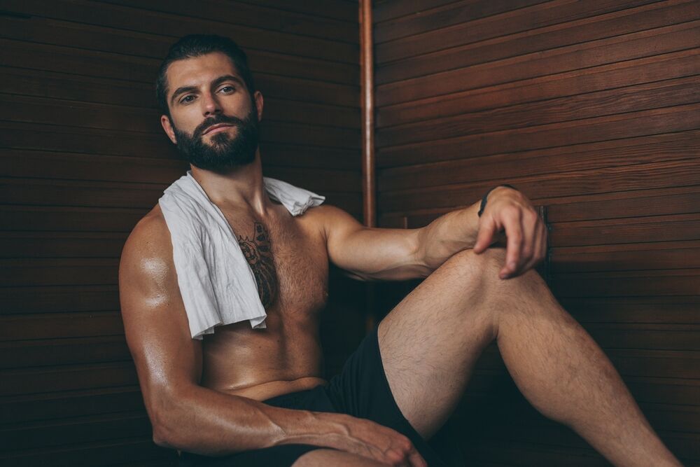 Fit male with tattoo and white towel, laying on the bench in the spa.