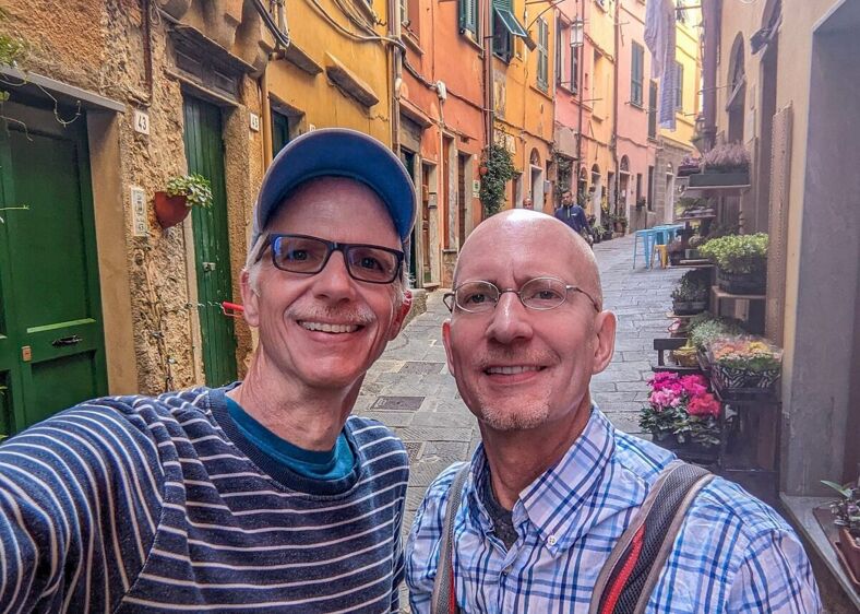 Michael Jensen and Brent Hartinger stand in a cobbled street lines with old buildings.