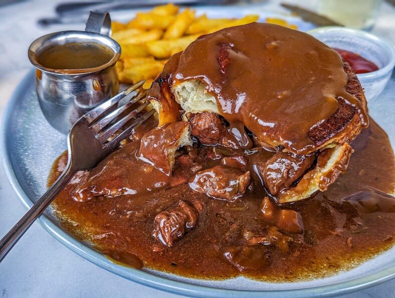 A meat pie soaked in gravy sitting on a plate with french fries.