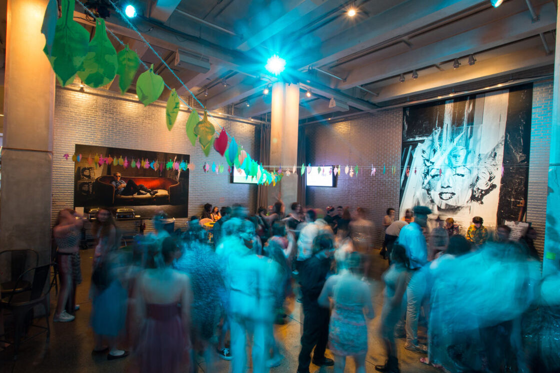 The entrance space to the museum is crowded with blurred participants for the annual Youth Prom. A Warhol painting of Marilyn Monroe hangs on the wall.