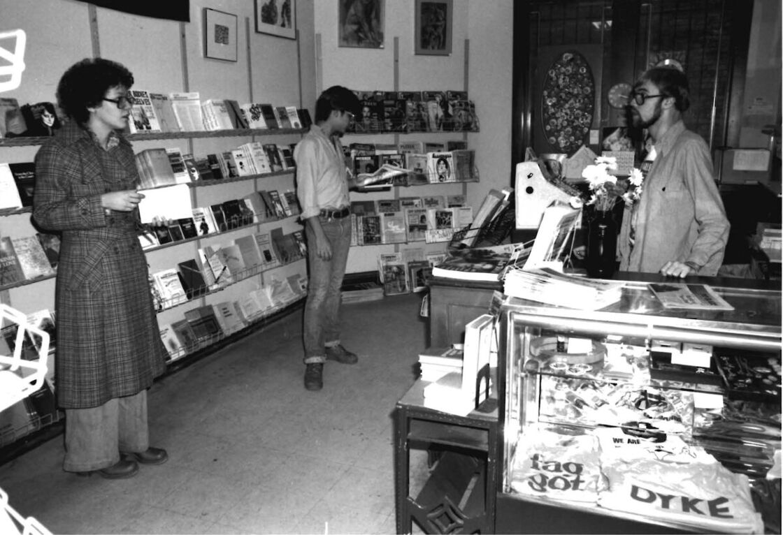 Two queer people checking out books near the register at Lambda Rising bookshop; there's a 