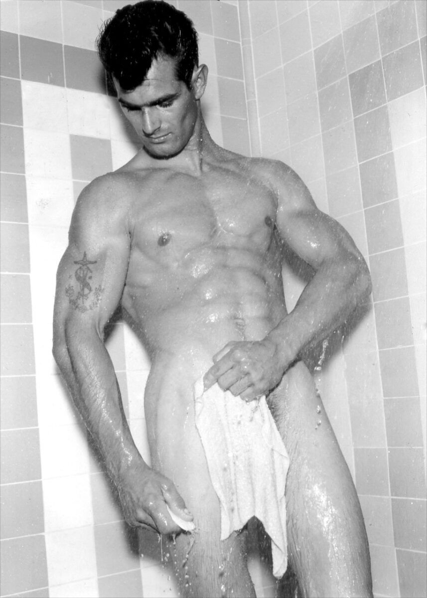 A young man with a Navy tattoo on his arm poses in the shower with a piece of cloth over his crotch