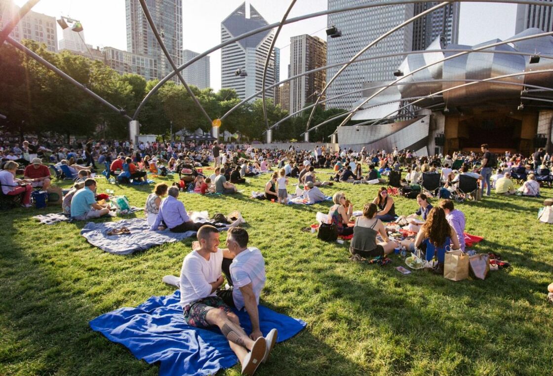 People picnic in a Chicago park. View of dozens of people sitting on blankets and snacking or snogging.