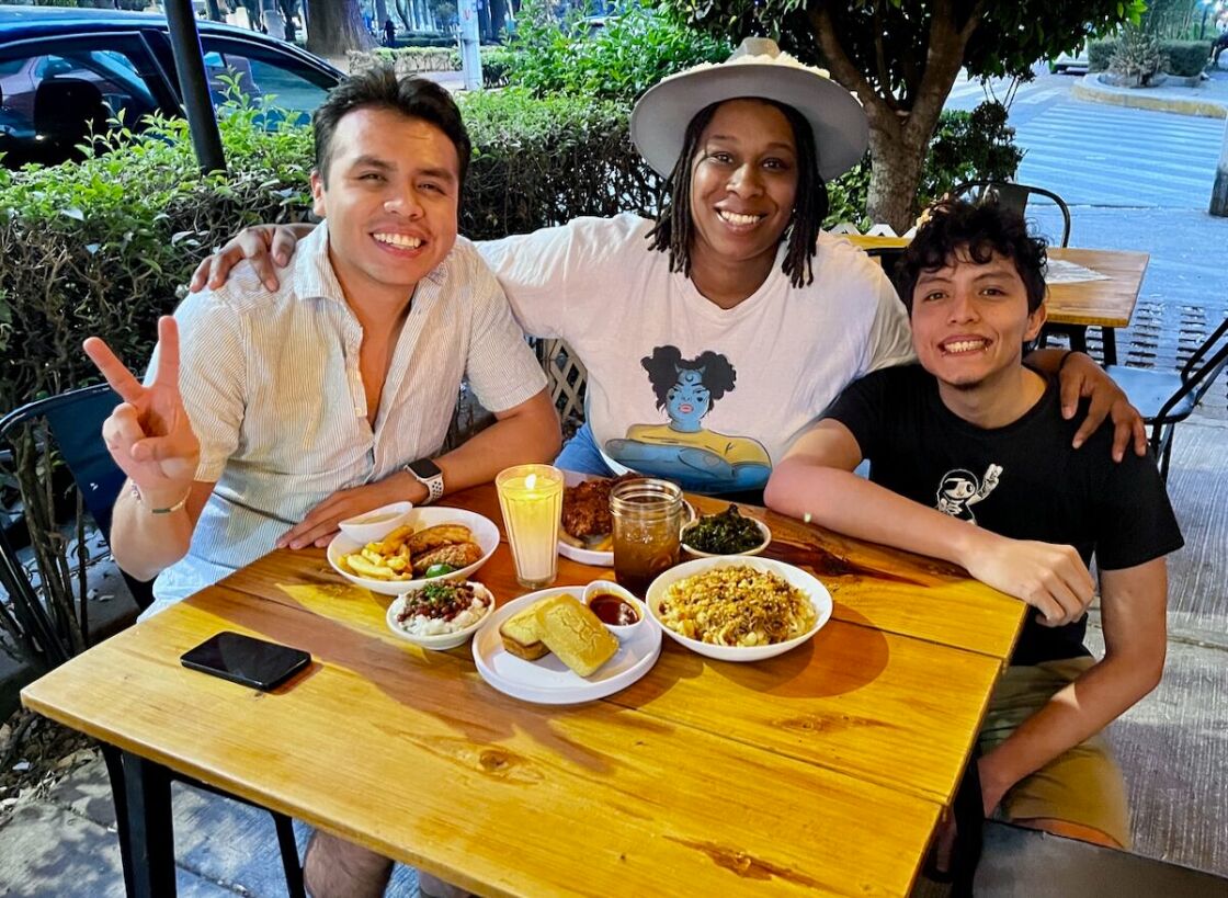 Uriel Zambrano, Tiara Darnell, and Dante Rico pose behind a table piled with soul food at Blaxicocina.