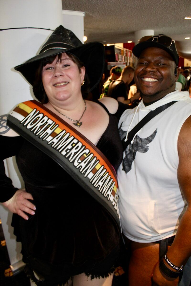 A woman dressed as a witch and wearing a sash that says "North American Mama Bear" stands next to an admirer.