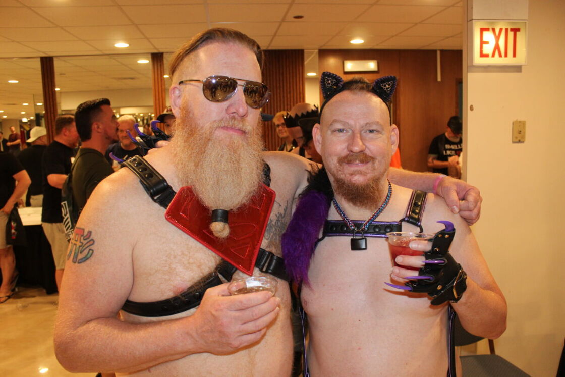 Two shirtless bears pose with cocktails in the hallway of IML.