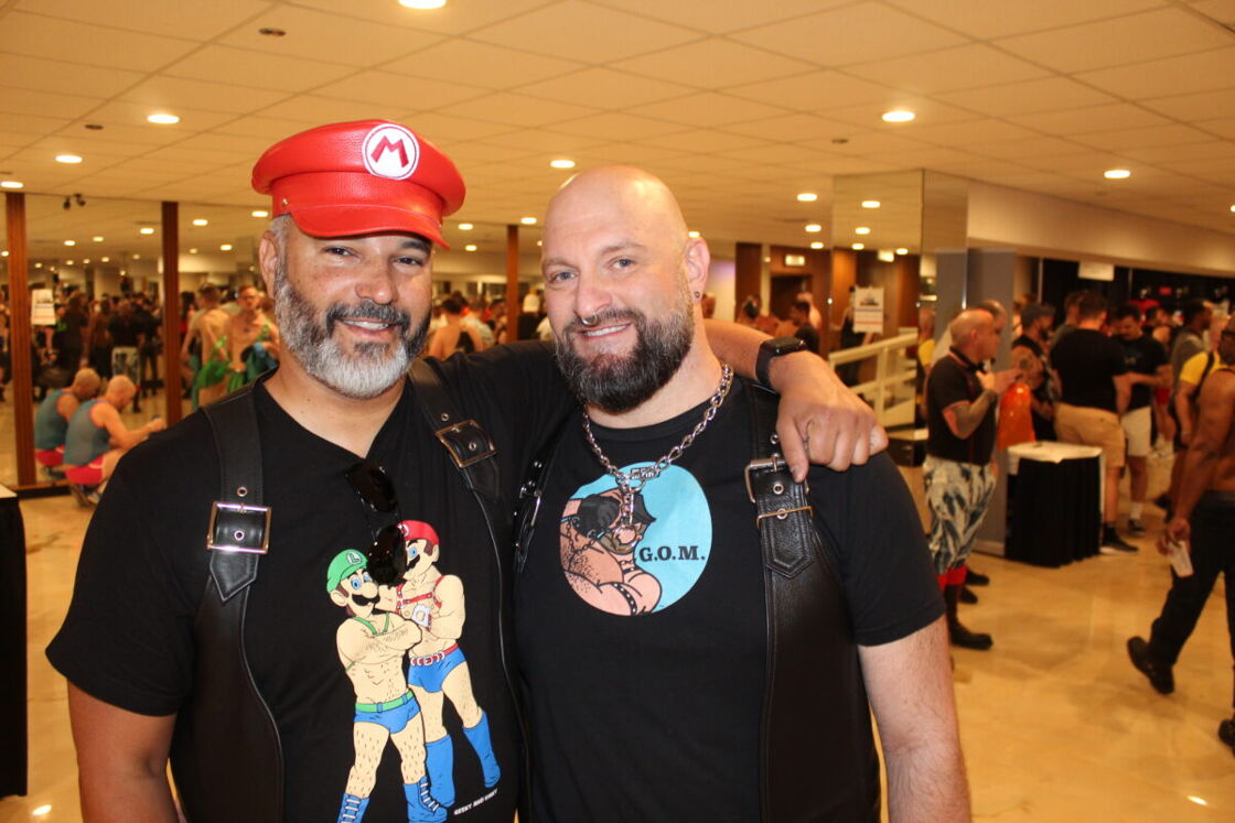 Two men, one wearing a Mario hat and the other a leather vest, pose for the camera.