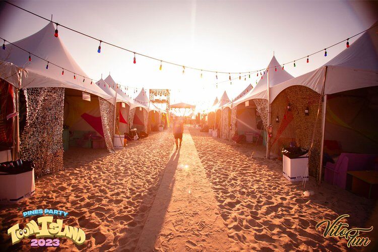 Beach tents lit up by a morning sunrise. Photo via Pines Party