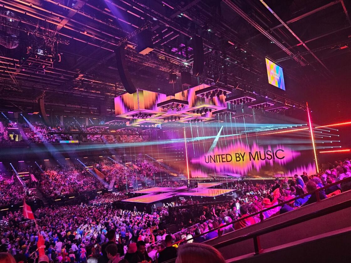 The view from inside the Malmö arena at Eurovision showing the stage and a background graphic that reads, "United By Music."