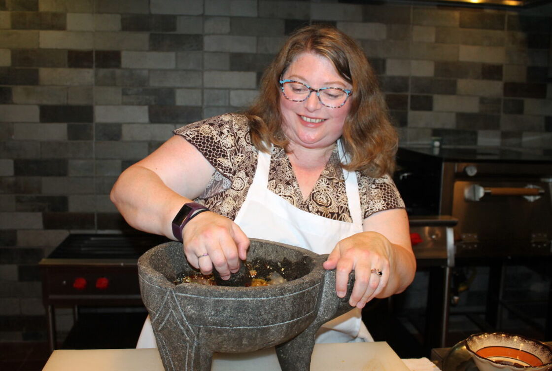 A woman smashes the tomatillos in a stone mortar and pestle in a cooking class at Oculto in Puerto Vallarta, Mexico.