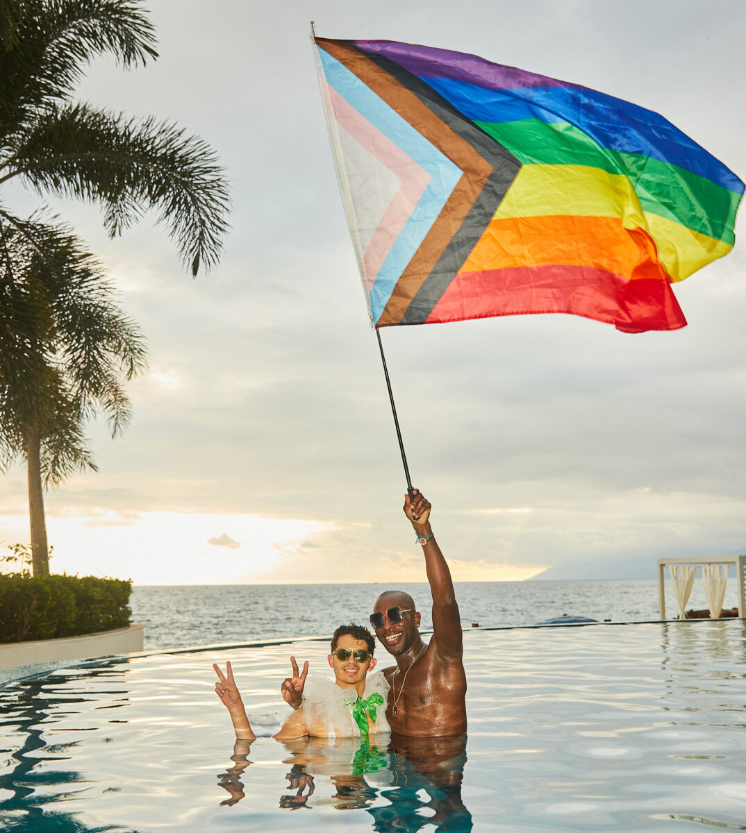 A gay couple holds a pride flag in a pool.