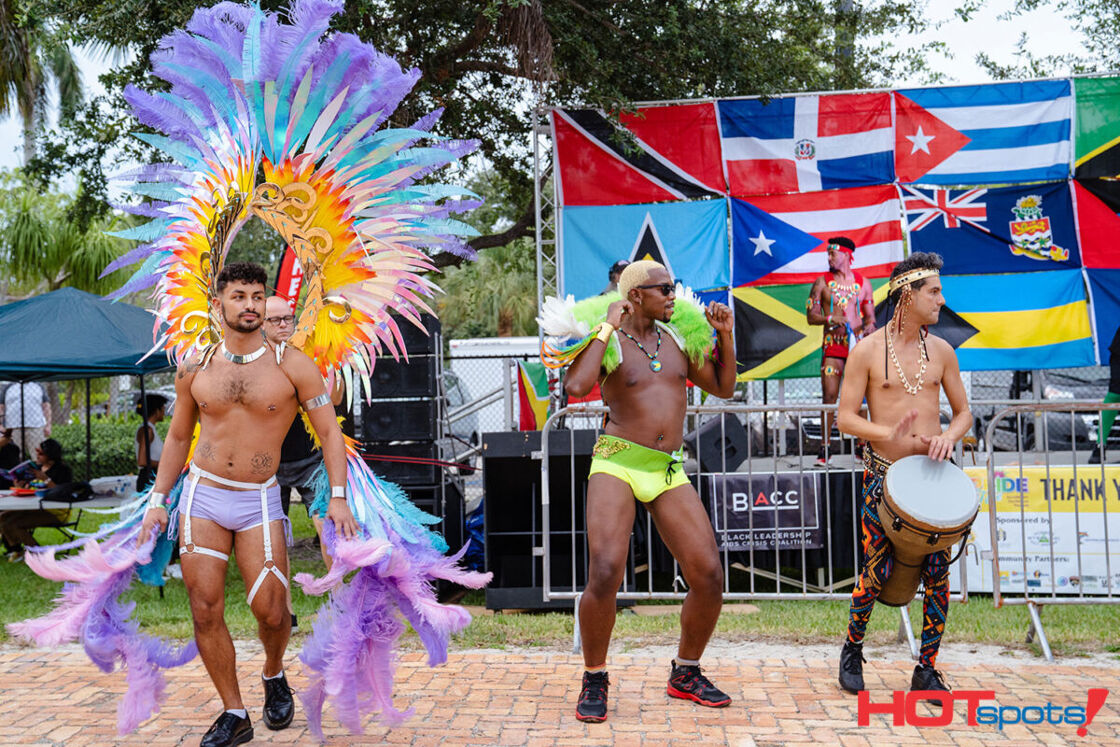 Male dancers, one with large plumes of feathers, another in a lime green swim suit and the third with a drum. Photo via PrideFete